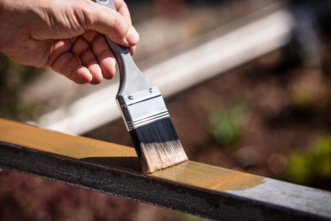 Mano aplicando barniz en barandilla metálica con una brocha