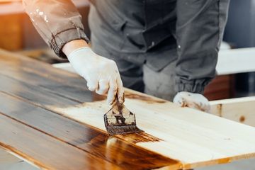 mano aplicando barniz sobre madera con una brocha